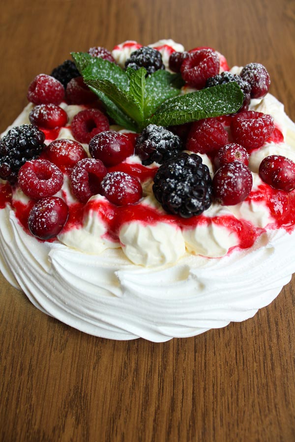 Vegan pavlova topped with mixed berries and a mint sprig