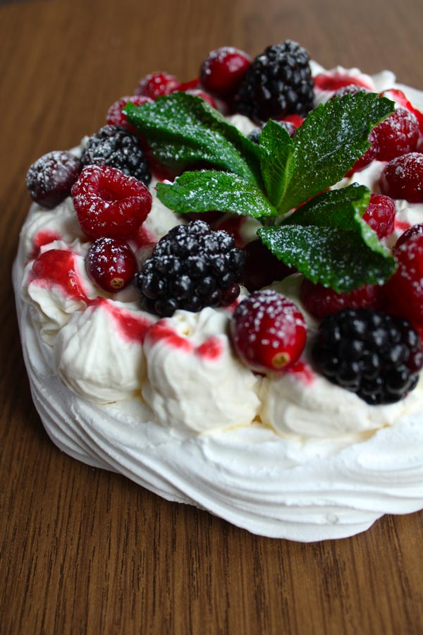 vegan pavlova with berries, whipped cream and a sprig of mint on top