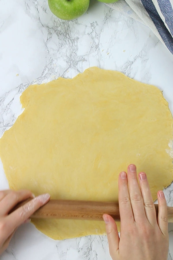 Hands using a rolling pin to roll out pastry on work top