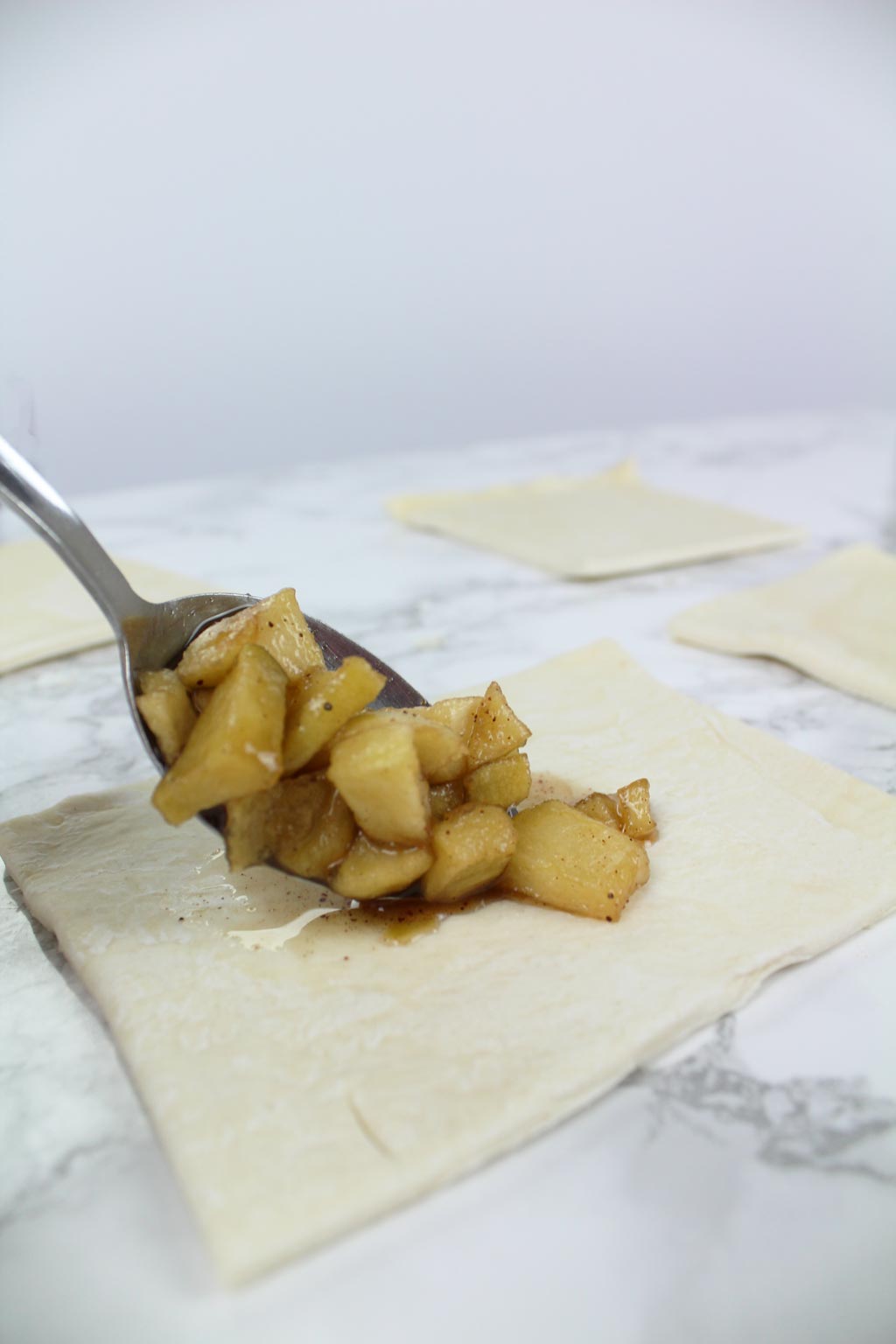 putting apple filling into puff pastry squares