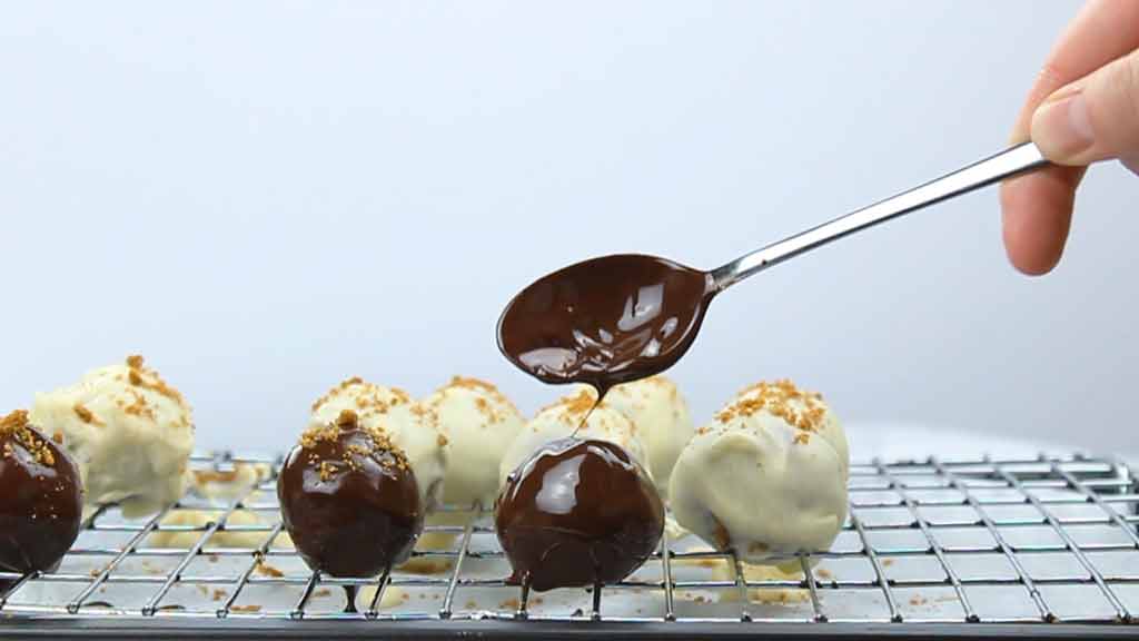 cheesecake bites on a wire rack being topped with chocolate