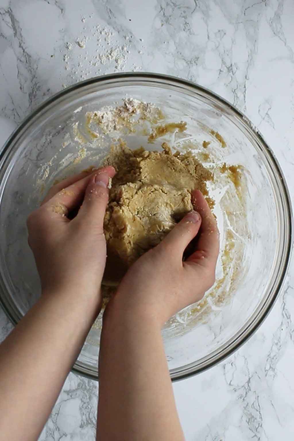 two hands holding a large ball of cookie dough in a bowl