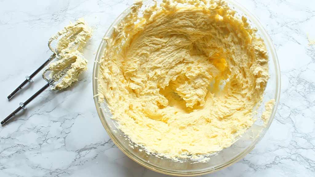 vegan butter and sugar creamed together in a large bowl, with two whisks beside the bowl