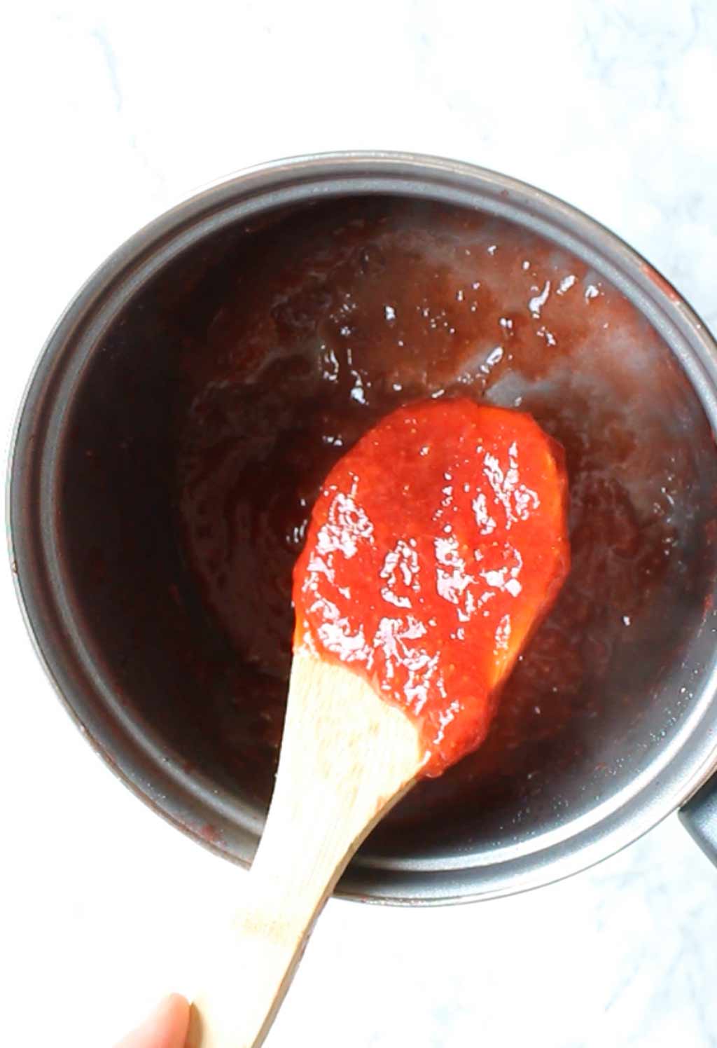 spoon holding the mashed strawberries over the pot