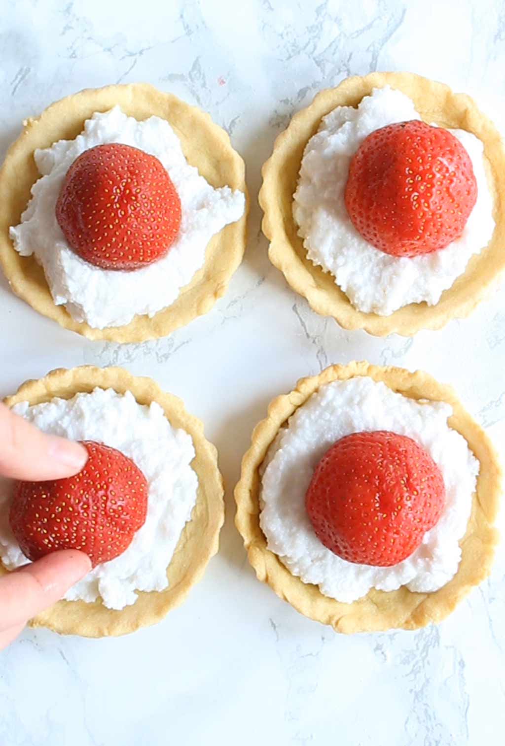 placing a strawberry on top of the cream on the tart