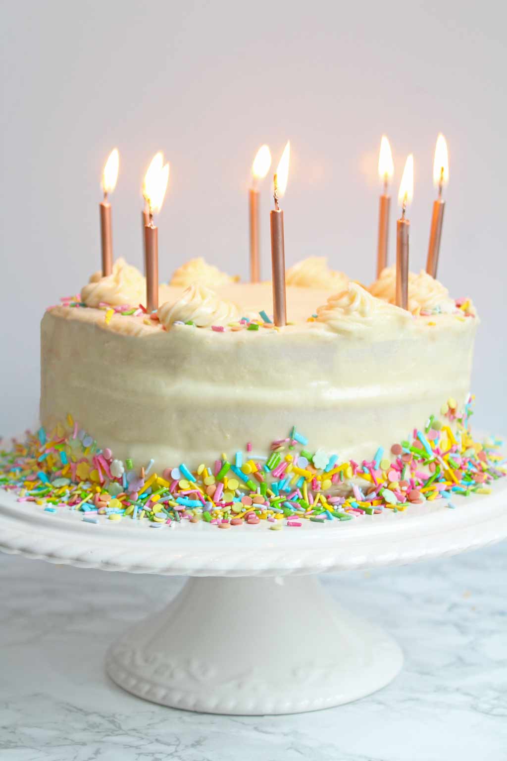 vegan birthday cake on a cake stand with candles lit