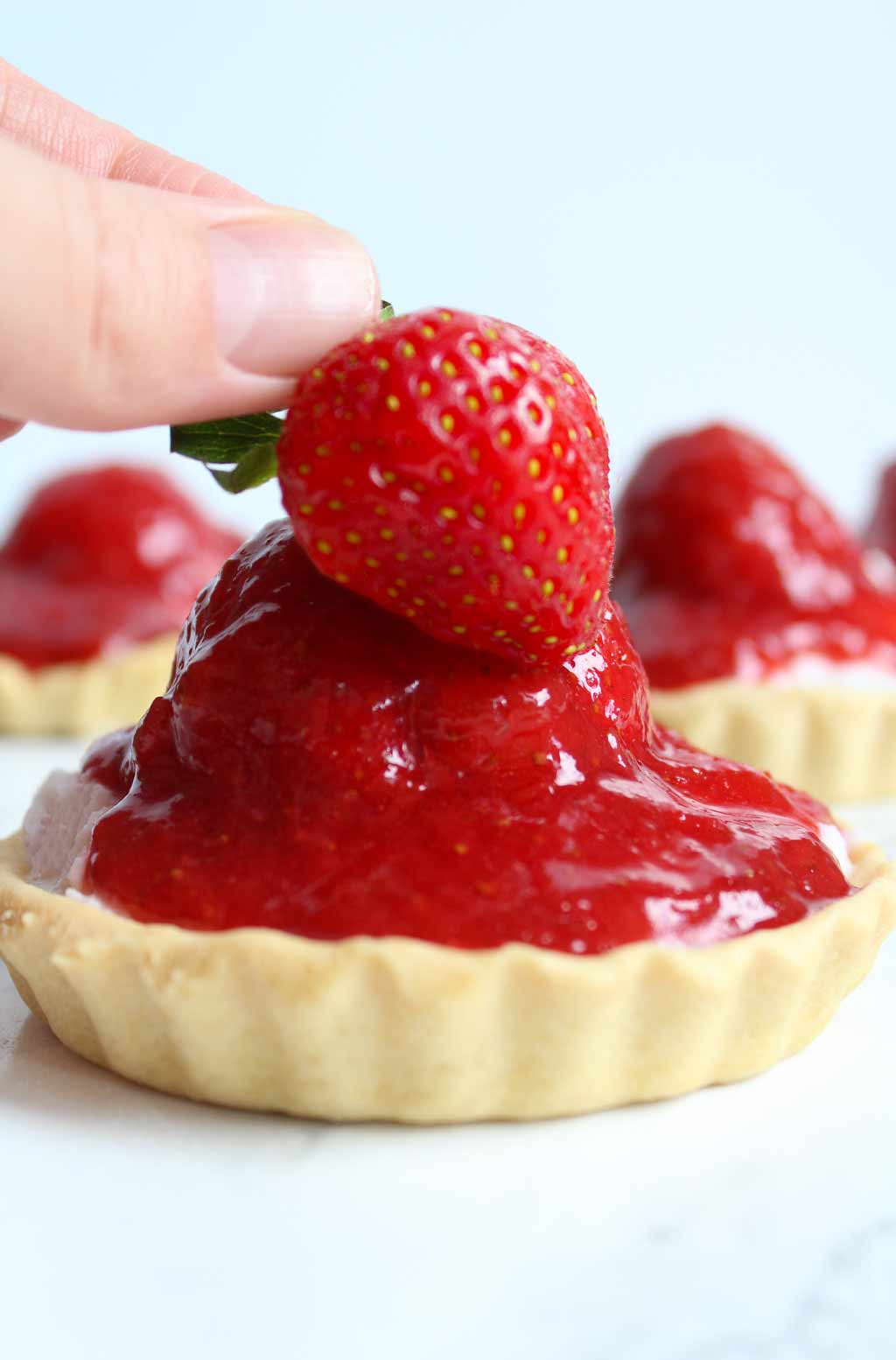 hand placing a strawberry onto the mini tart