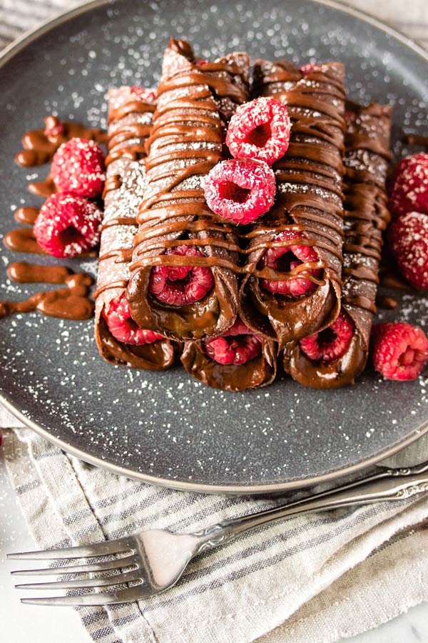 a plate of chocolate crepes with raspberries on top