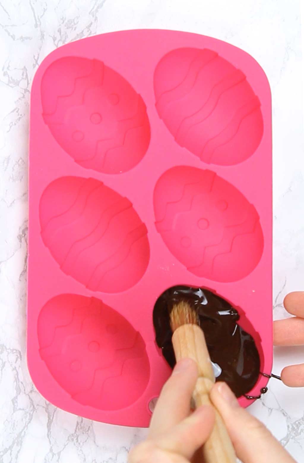 using a pastry brush to spread chocolate into the egg mold