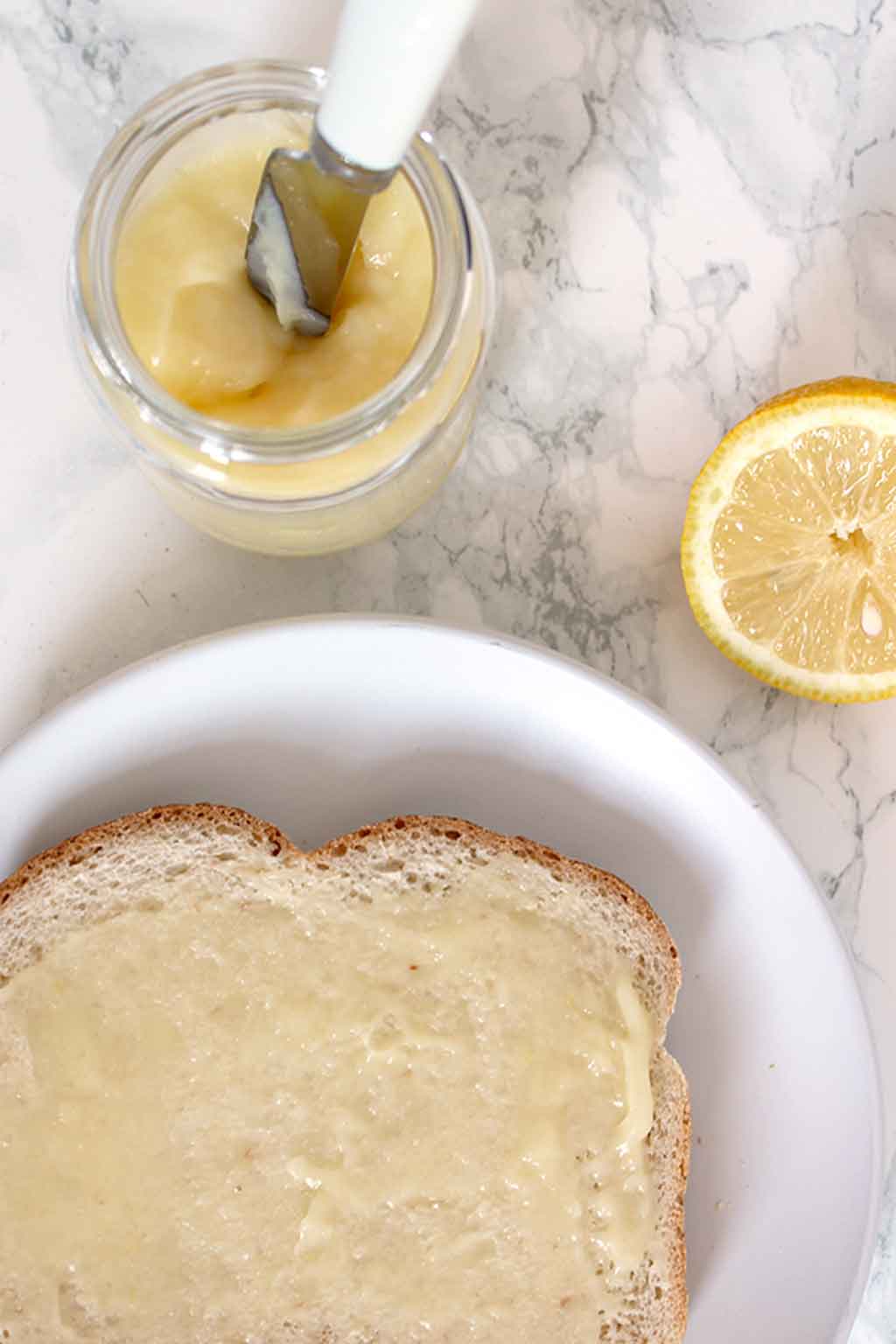 a piece of bread with lemon curd spread on it beside a jar of lemon curd