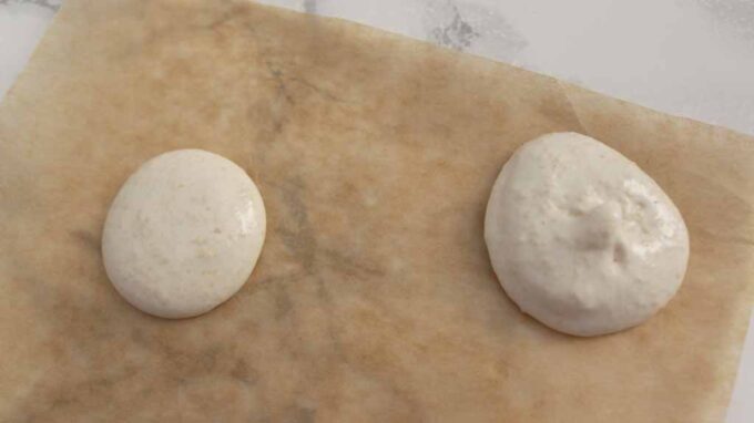 Two Macarons On A Sheet Of Baking Paper. The left one is ready and the right one is undermixed.