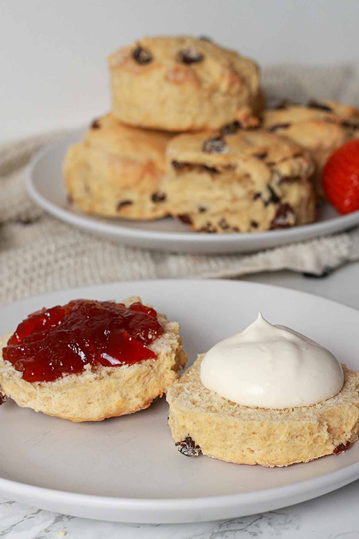 Vegan fruit scones. Cut In Half. One Half Is Topped With Cream And The Other Half Is Topped With Jam.