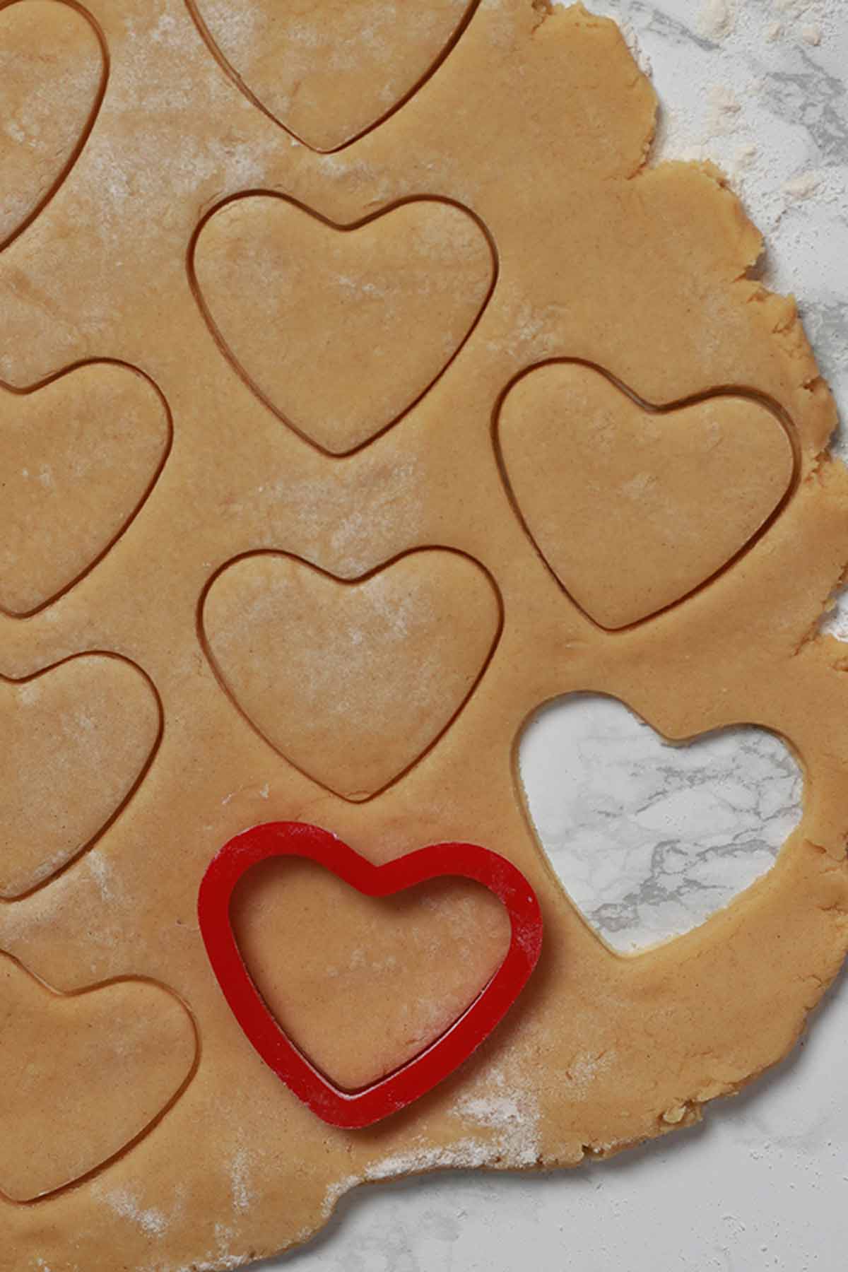eggless valentines cookie dough rolled out and being cut into love heart shapes