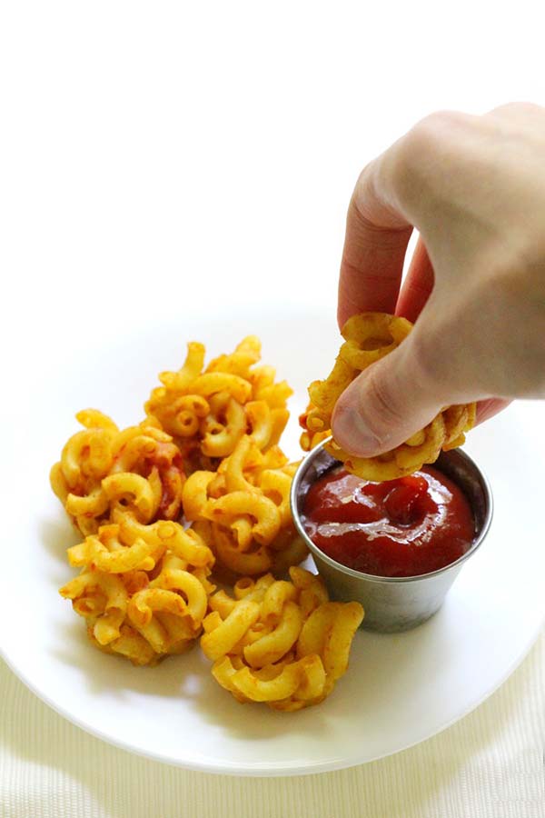 Hand dipping mac and cheese bite into tomato sauce
