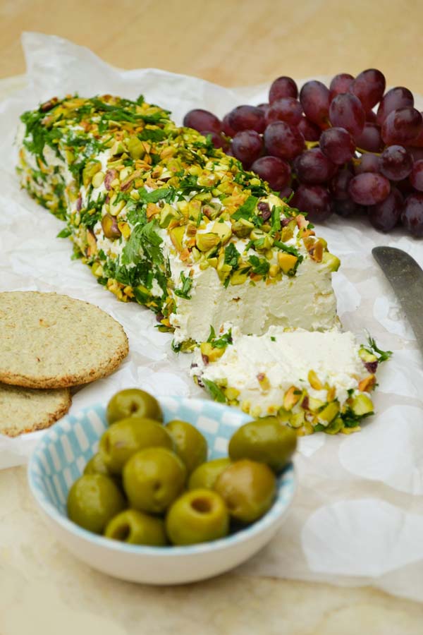 Cheese log topped with pistachios, beside some olives, oatcakes and grapes