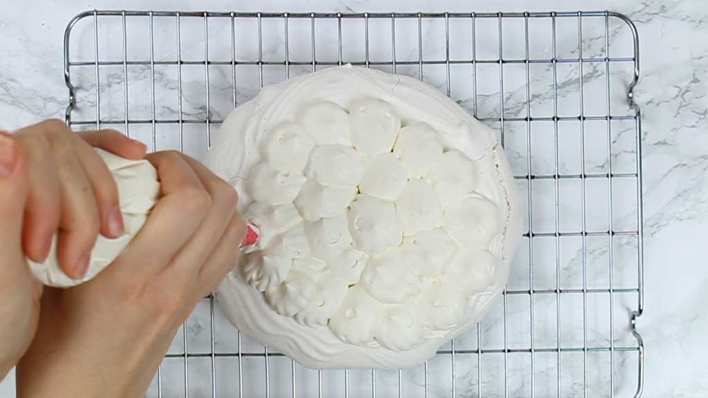 piping whipped cream onto the pavlova