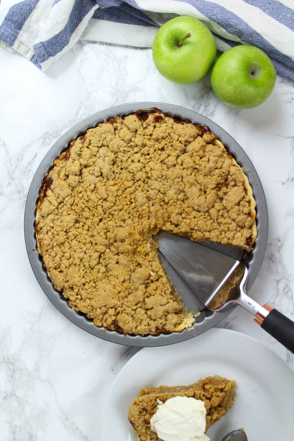 Overhead shot of Vegan Dutch apple pie in the tin with one slice cut out. The slice is beside the tin on a plate and is topped with ice cream