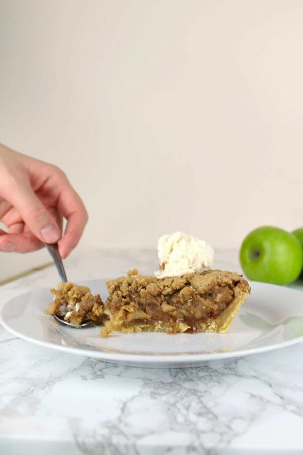 spoon cutting into a slice of vegan apple crumble pie on a plate