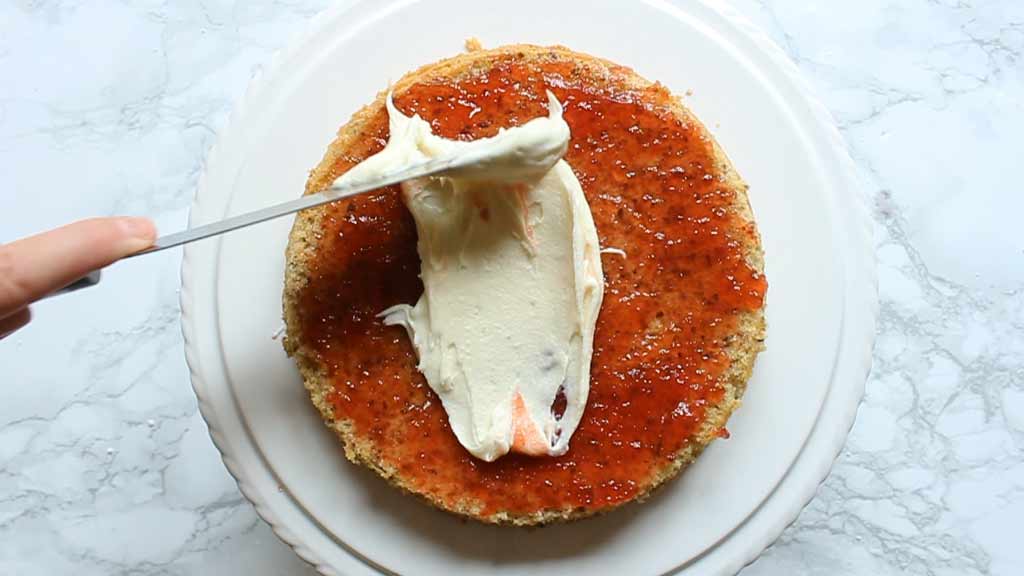 spreading jam and vanilla frosting on top of the sponge cake