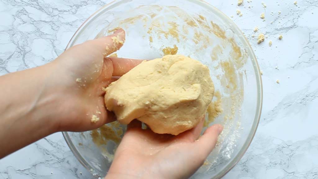 two hands holding shortbread dough in the bowl