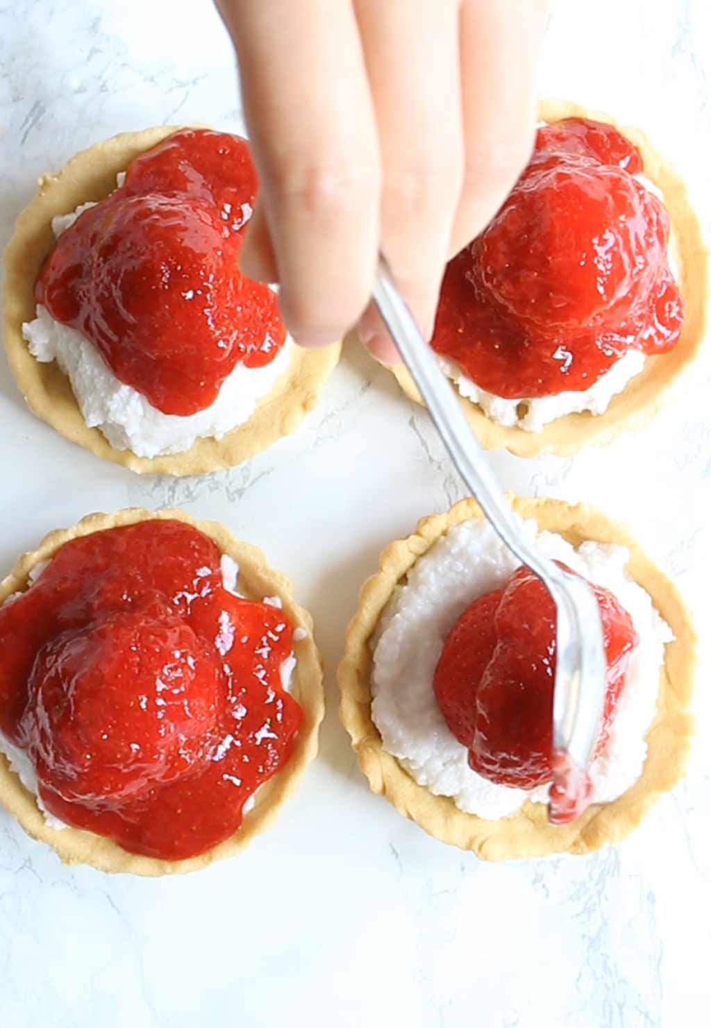spooning strawberry glaze onto the tarts