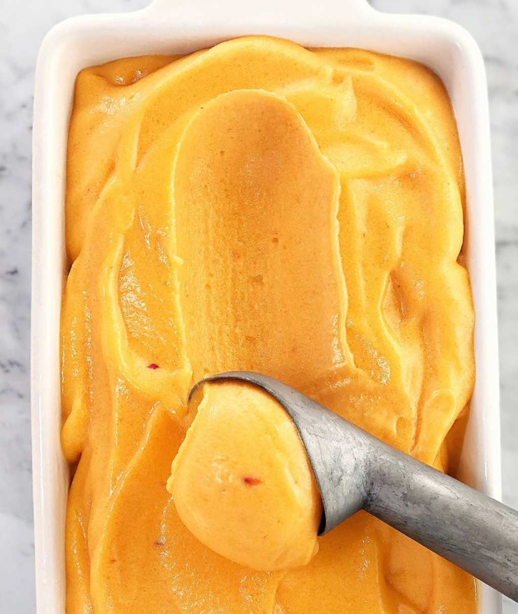 peach sorbet in a tub with a scoop in it