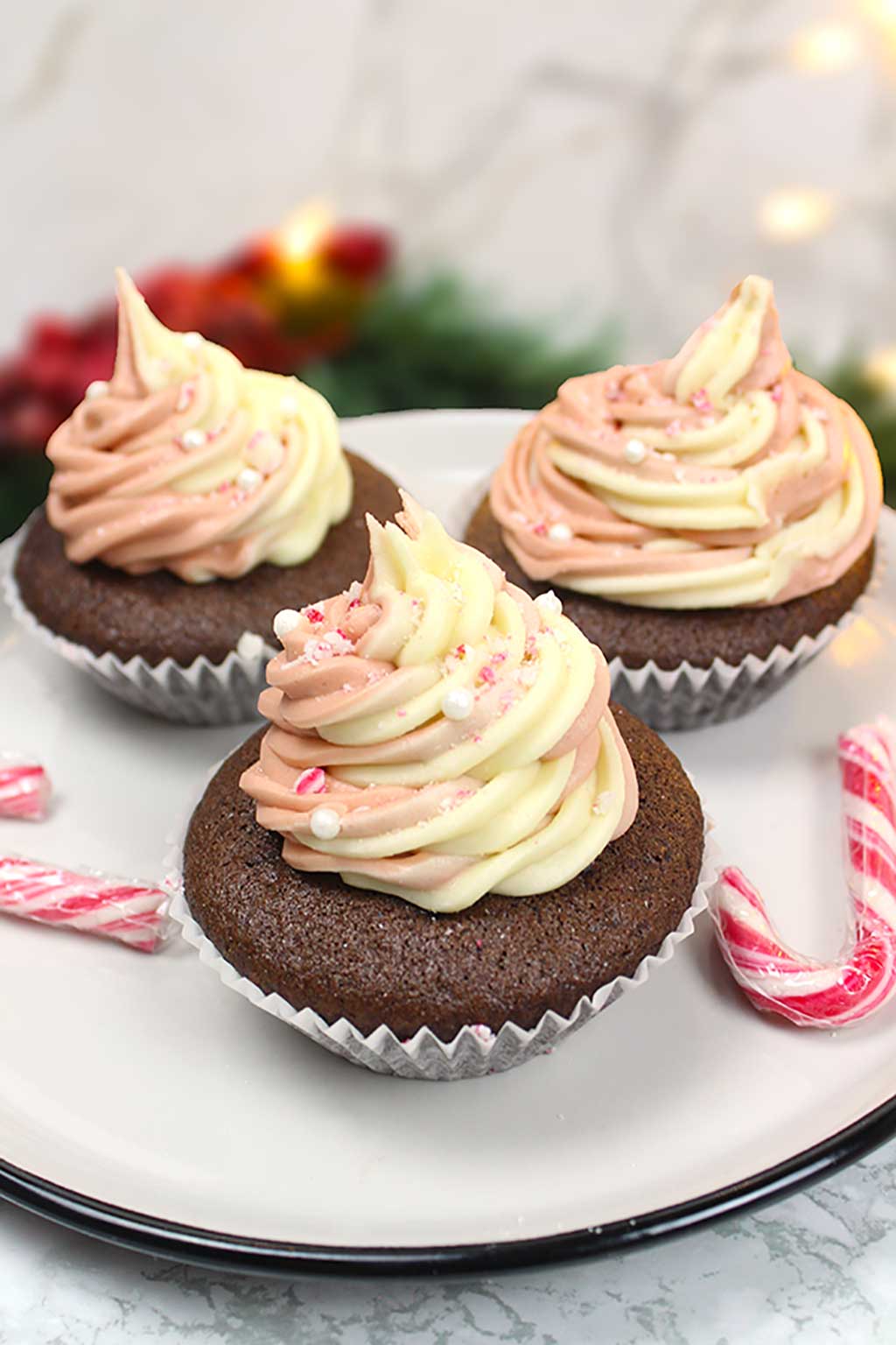 3 vegan candy cane cupcakes on a plate along with 2 mini candy canes