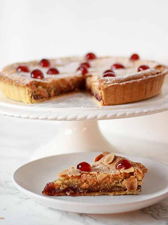 Thumbnail of cherry bakewell tart on a cake stand, with one slice on a plate in front