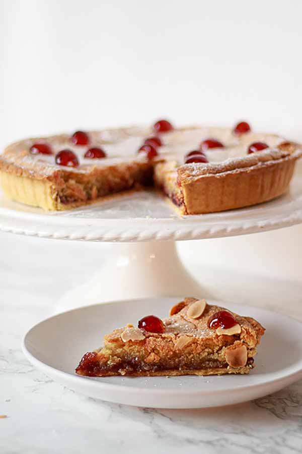 Thumbnail of cherry bakewell tart on a cake stand, with one slice on a plate in front