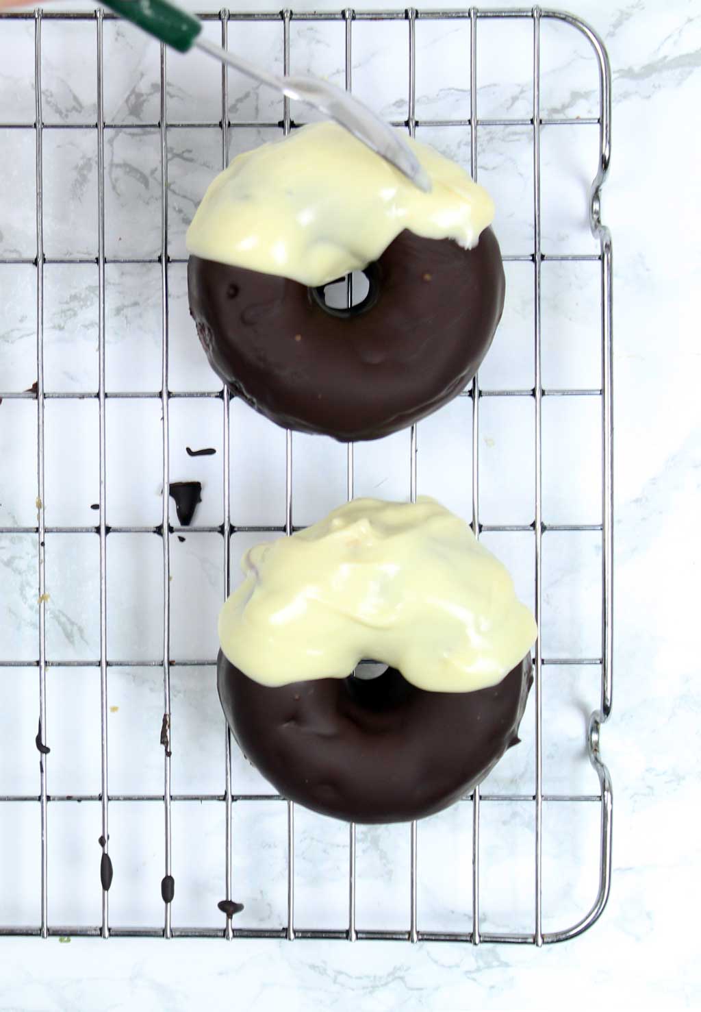 spooning white chocolate onto the donuts