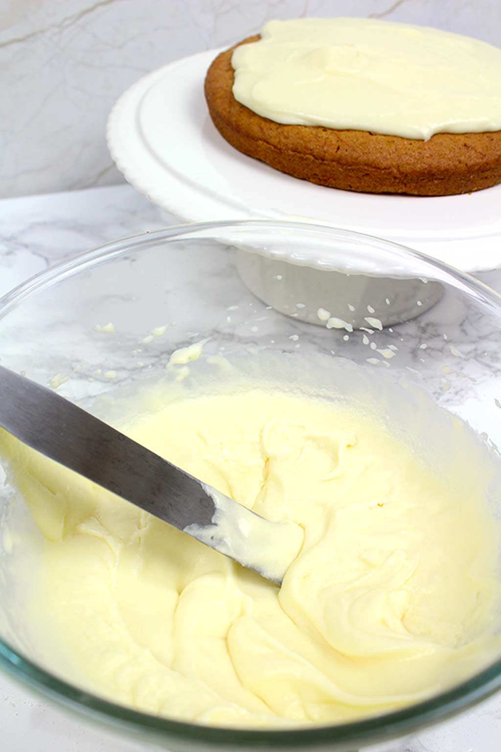 cream cheese frosting in a bowl with a frosted cake in the background