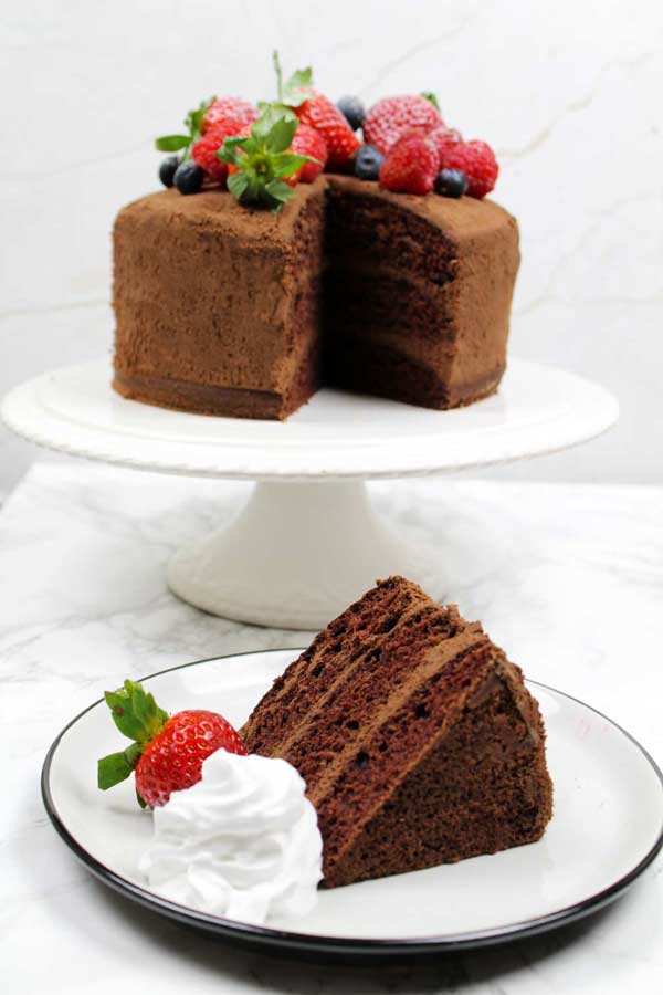 slice of vegan chocolate cake on a plate with rest of cake in background