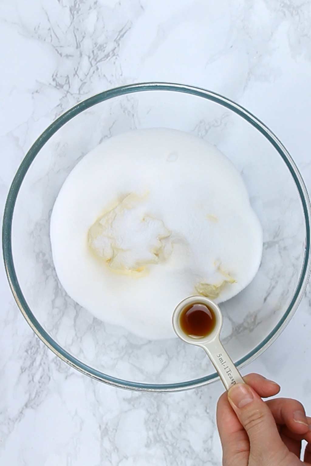 teaspoon of vanilla over bowl containing sugar and vegan butter