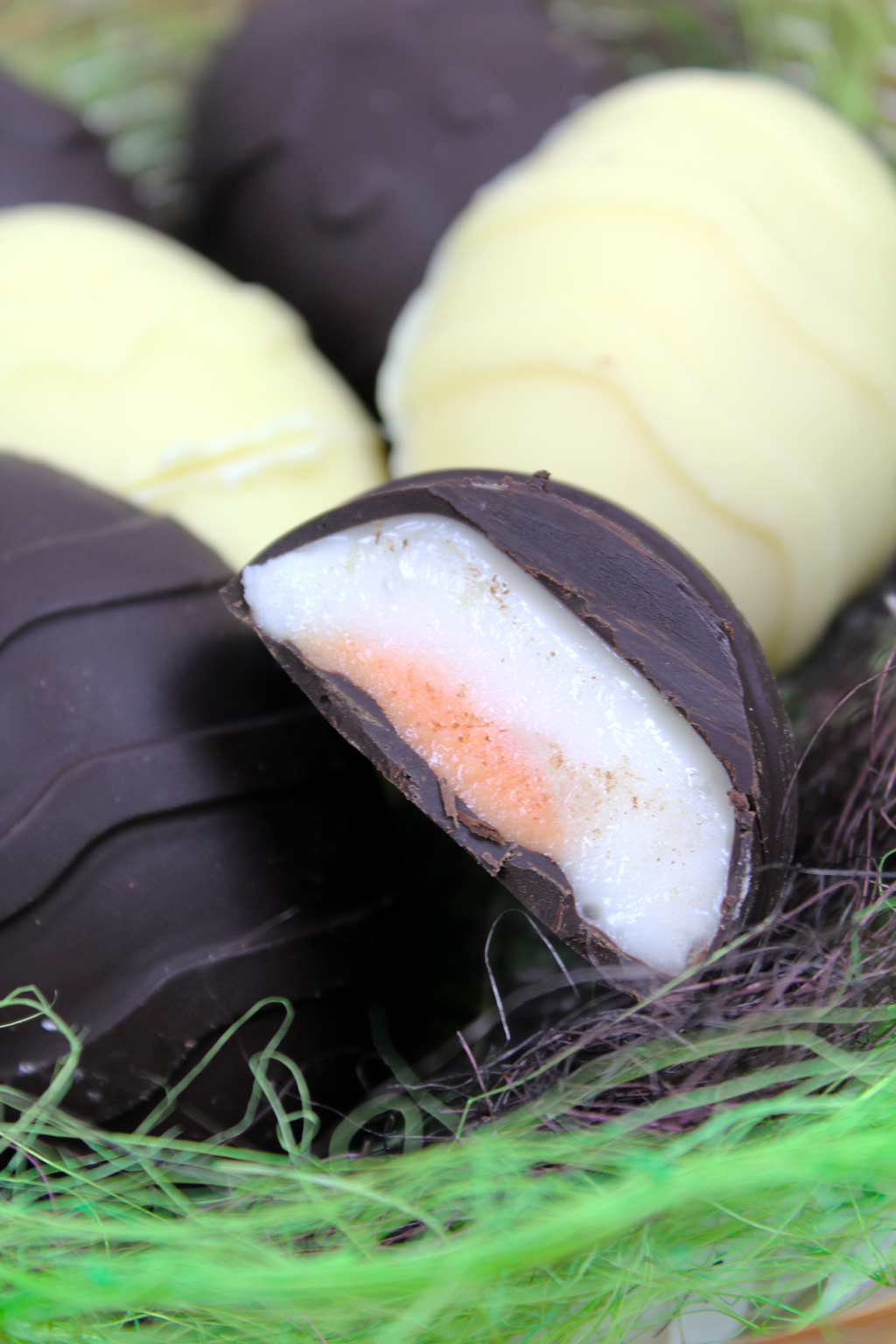 A basket full of vegan creme eggs. One at the front is cut in half to show the fondant filling.