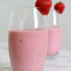 two strawberry milkshakes in glasses with a strawberry sitting on the rim of each glass