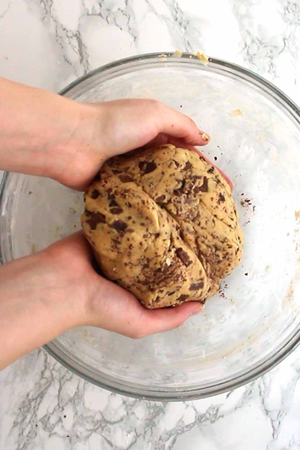 hands holding a ball of chocolate chip cookie dough
