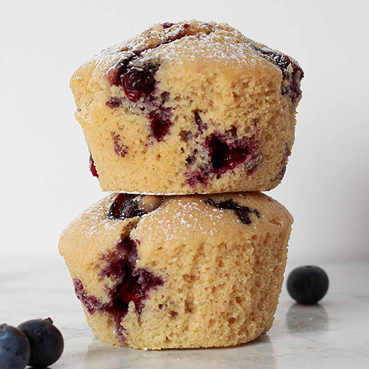 2 Eggless Blueberry Muffins Stacked On Top Of One Another