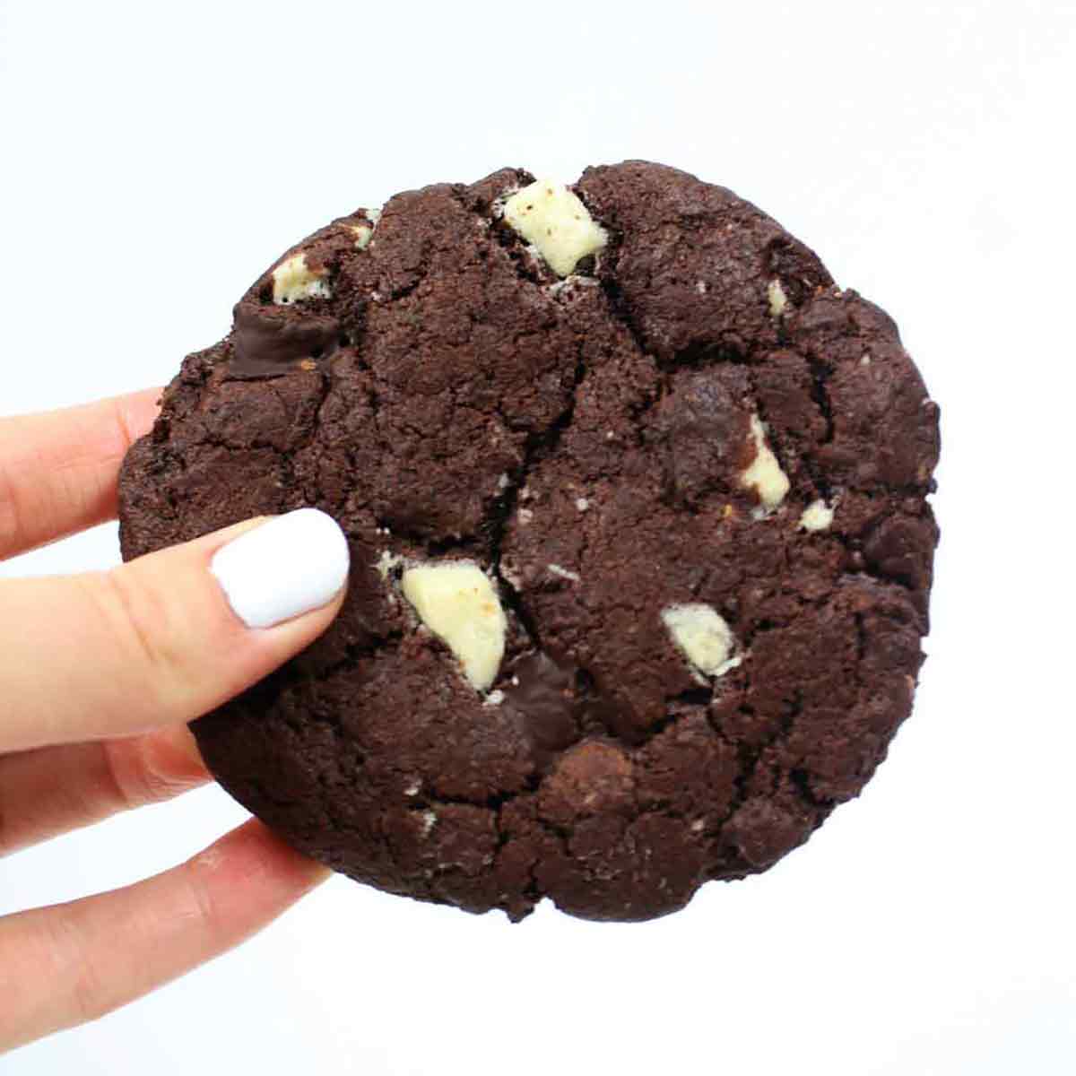 A Vegan Double Chocolate Chip Cookie Being Held Up By A Hand