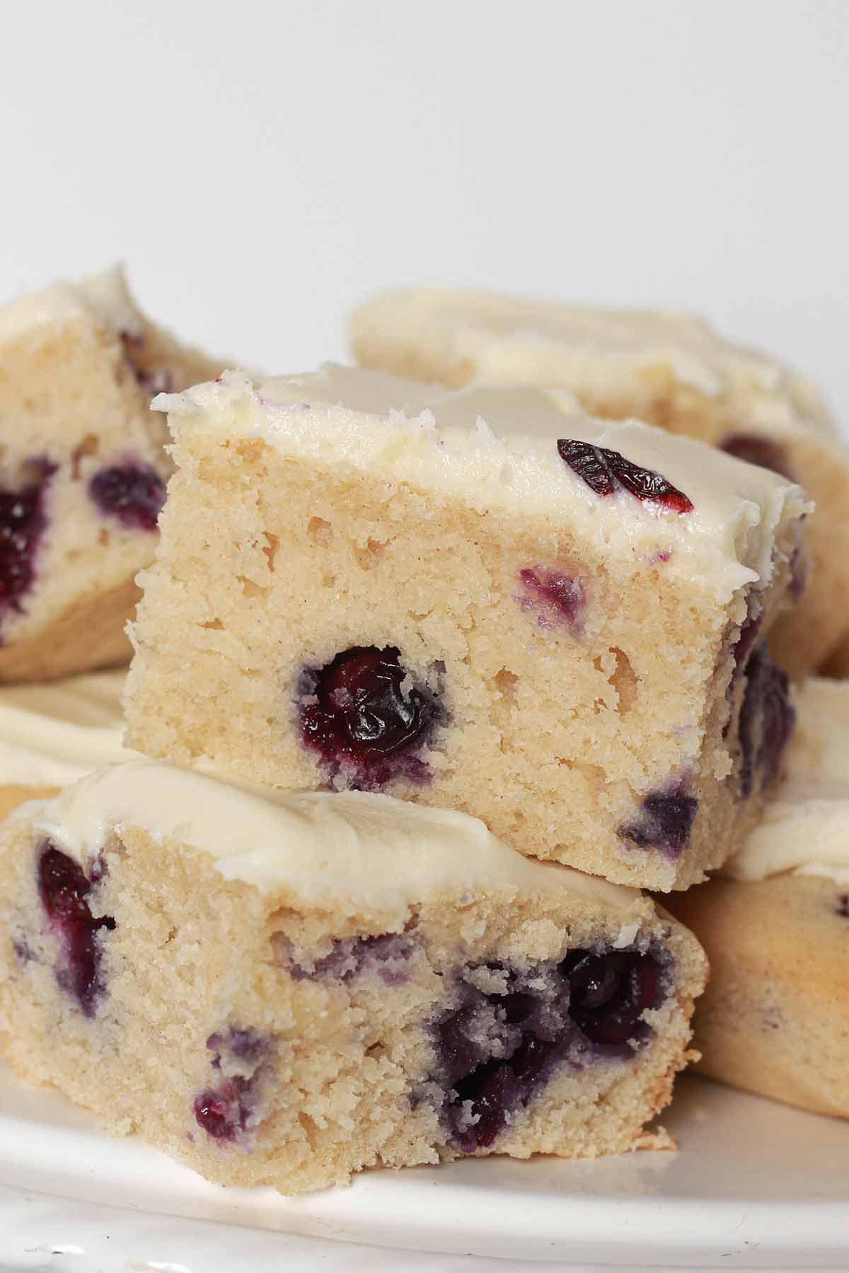 Eggless Blueberry Cake Slices Piled Up On A Plate with lemon cream cheese frosting on top
