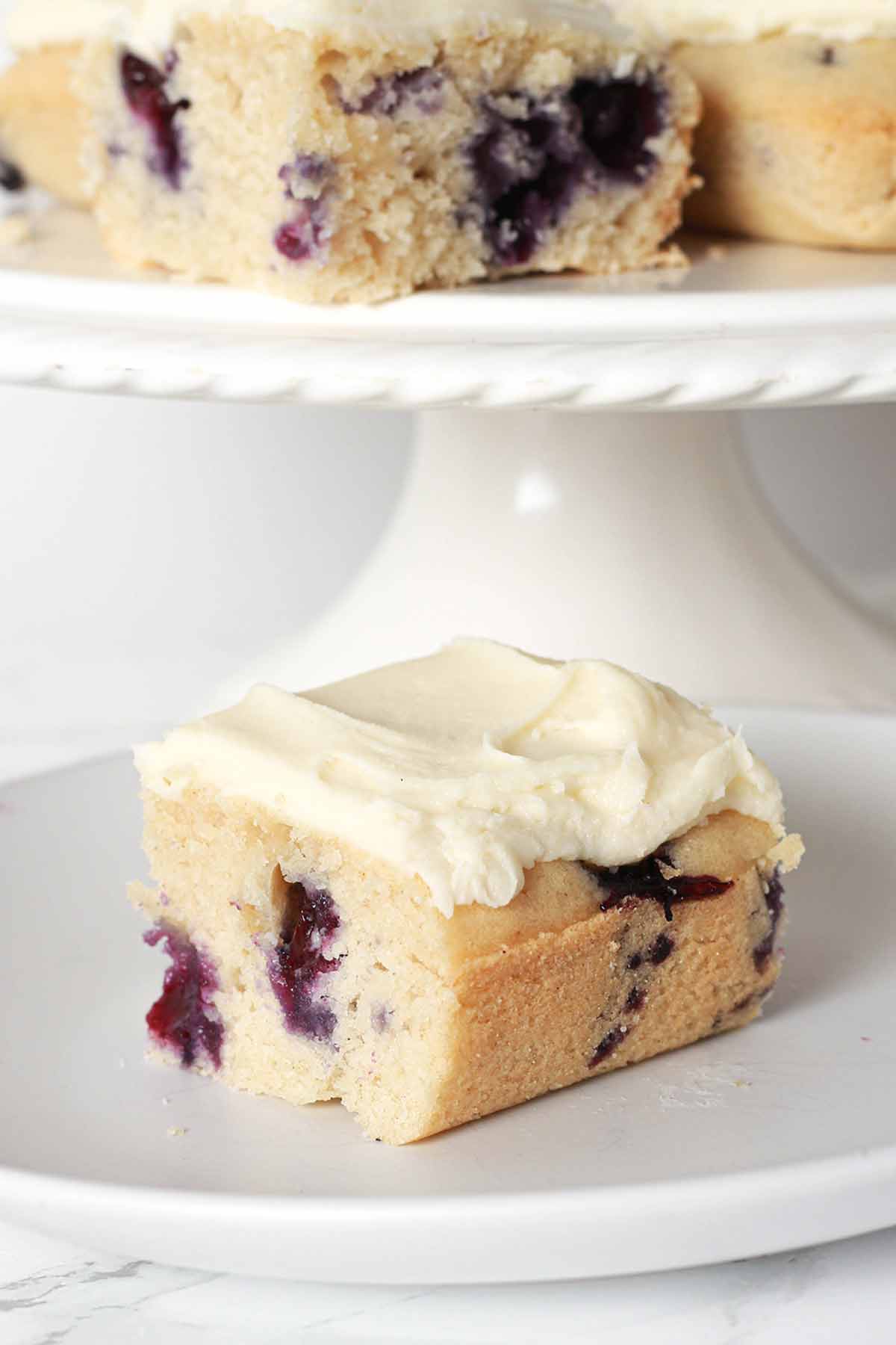 Slices Of Blueberry Cake On A Cake Stand Behind A Slice On A Plate