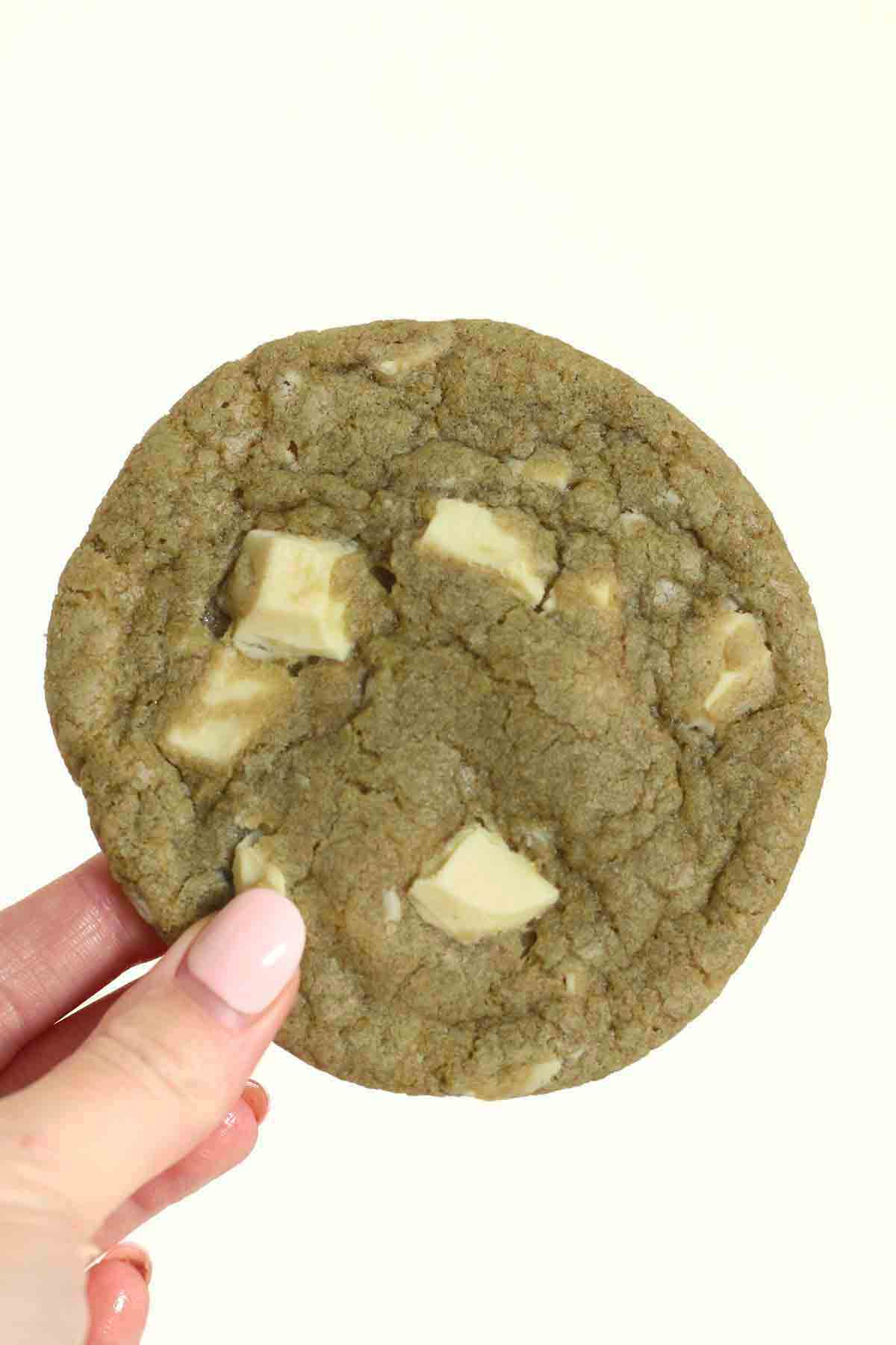 Hand Holding Up An Eggless Matcha White Chocolate Cookie